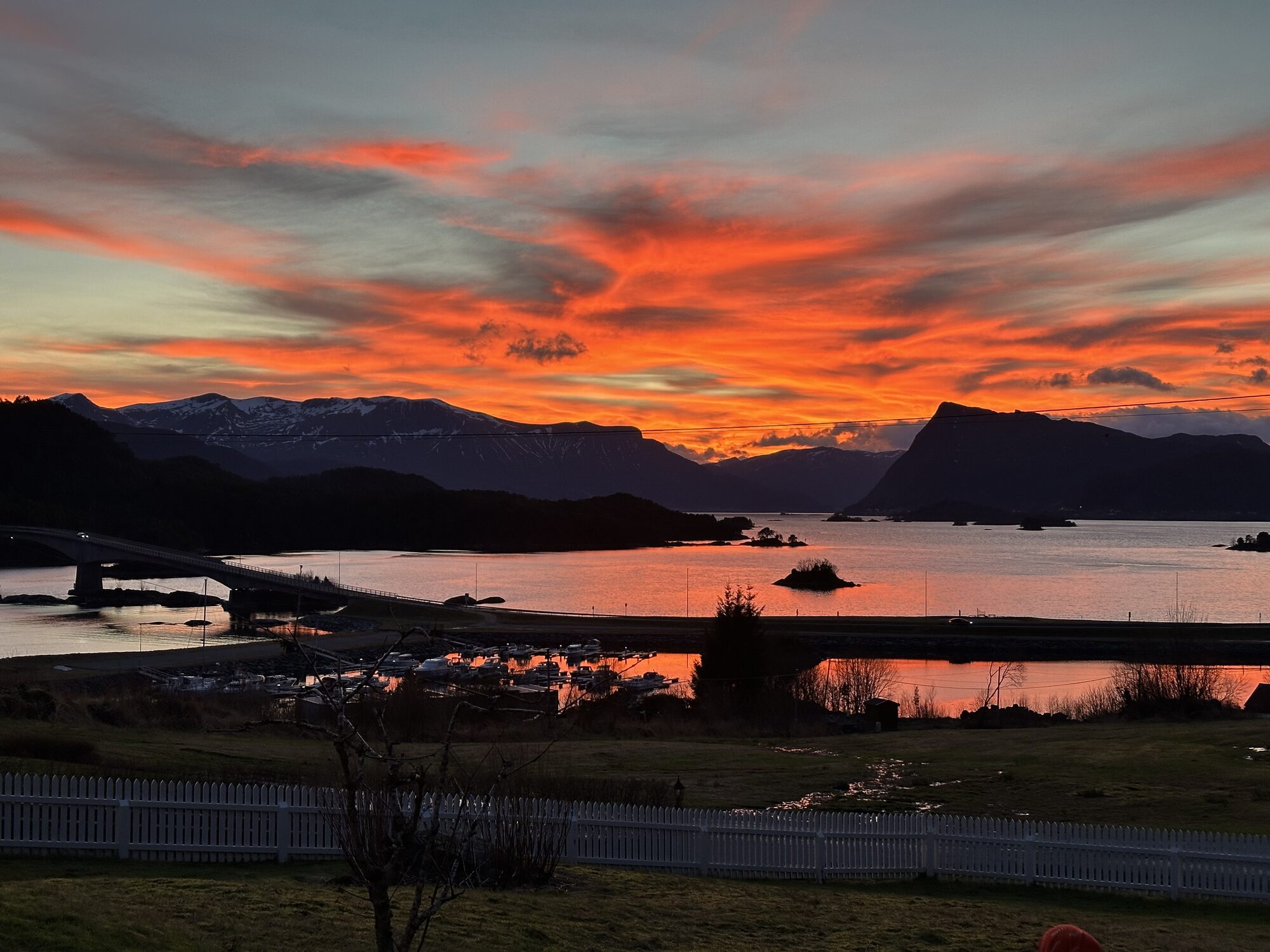 Dramatisk oransje solnedgang over Eiksundbrua og båthamna